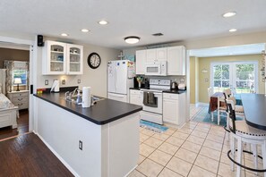 A modern kitchen with white cabinetry, a black countertop, and a dining area with a table and chairs. - 3 BR Pool Home In Nokomis - Close To Beaches - Tropical Escape (Nokomis)