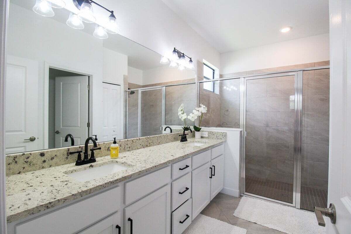 A modern bathroom with a large mirror, granite countertop, and a walk-in shower.
