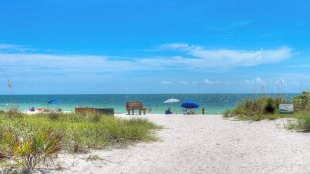 A beach with a sandy path leading to the water, a wooden bench, and a sign indicating a protected area. - Cozy 2BR condo on Lido Key, steps from the beach - Lido Del Mare (Sarasota)