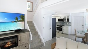 A modern living room with a TV, fireplace, and a staircase leading to a kitchen and dining area. - Cozy 2BR condo on Lido Key, steps from the beach - Lido Del Mare (Sarasota)