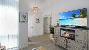 A living room with a flat-screen TV, a fireplace, and a view of a beach. - Cozy 2BR condo on Lido Key, steps from the beach - Lido Del Mare (Sarasota)