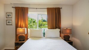 Habitación de hotel con una cama grande, dos lámparas de noche, una ventana con cortinas y cuadros en la pared.