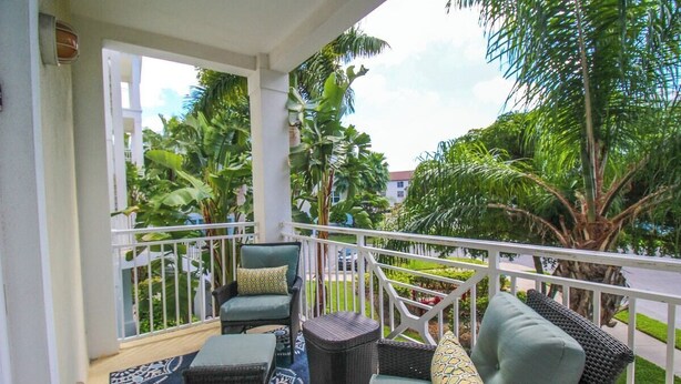 A balcony with wicker furniture, a patterned rug, and lush greenery in the background.