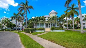 A hotel with a central building, surrounded by palm trees and a well-maintained lawn.