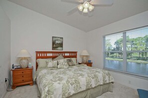 A bedroom with a bed, nightstands, a ceiling fan, a window with blinds, and a painting on the wall. - Golf course view - 2BR - 2nd floor condo - Eagle Hunters (Sarasota)