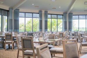 Un vaste espace dédié à la salle à manger, avec de nombreuses tables et chaises, de grandes fenêtres dotées de rideaux et une vue sur la verdure environnante.