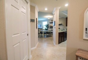 Un pasillo que conduce a un comedor con una mesa y sillas, una cocina con armarios y un fregadero, y una puerta a la izquierda.