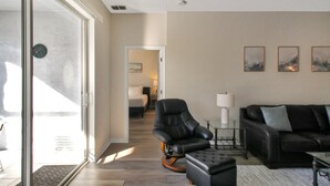A modern living room with a glass door leading to a balcony, a black leather sofa, a black armchair, and a small table with a lamp. - Luxurious 4BR 2BA home with pool Bradenton My Great Escape (Bradenton)