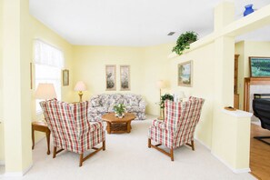 A living room with a floral sofa, two plaid armchairs, a coffee table, and a fireplace.