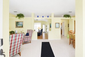 A spacious living area with a dining table, two armchairs, a black rug, and a view into the kitchen.