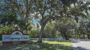 Un letrero de Regency Oaks, con una cerca blanca y árboles al fondo.