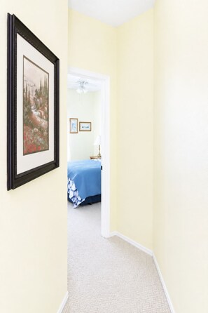 A hallway leading to a bedroom with a bed and a framed picture on the wall.