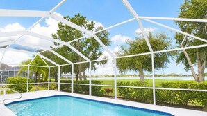 Una piscina con estructura de techo blanco, rodeada de follaje y árboles.