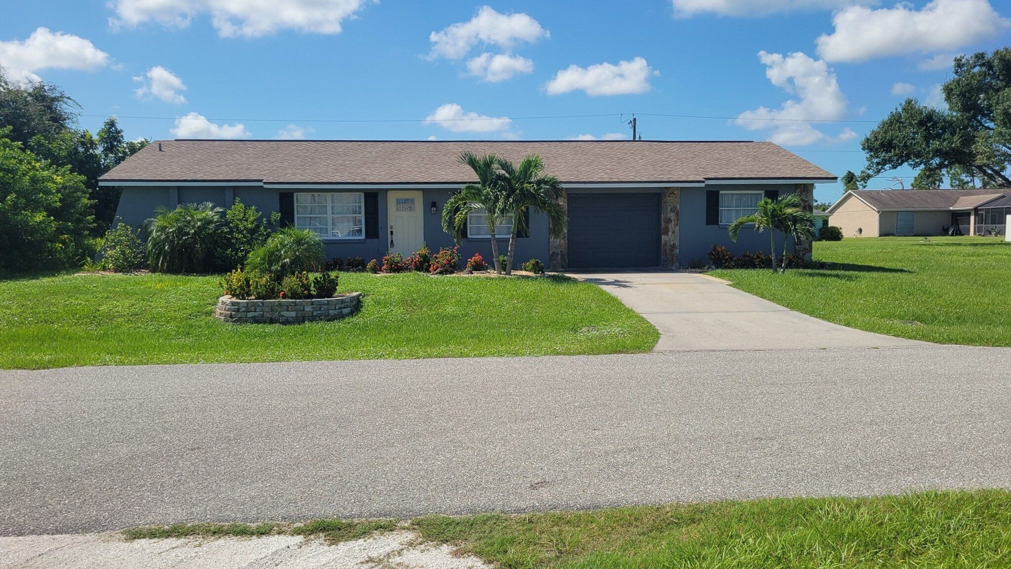 A single-story house with a grey roof, a front yard with a stone planter, and a clear sky.