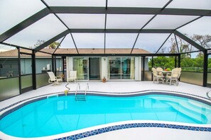 A covered swimming pool with a tiled edge, surrounded by a glass enclosure, and furnished with outdoor chairs and a table. - Relaxing pool home in Englewood - Awake Zone (Englewood)