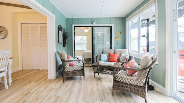A room with wicker furniture, a wooden floor, a white door, and a view through a glass door. - Gorgeous 2BR 2BA Private Pool Home Near Siesta Key Sweet Pineapple (Sarasota)