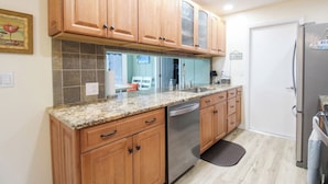 A kitchen with wooden cabinets, a granite countertop, a dishwasher, and a refrigerator. - Gorgeous 2BR 2BA Private Pool Home Near Siesta Key Sweet Pineapple (Sarasota)