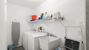 A laundry area with a washing machine, dryer, and a shelf with cleaning supplies. - Relaxing 2BR - Pool home close to attractions - Charlotte's Dream (Port Charlotte)