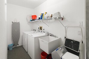 A laundry area with a washing machine, dryer, and a shelf with cleaning supplies. - Relaxing 2BR - Pool home close to attractions - Charlotte's Dream (Port Charlotte)