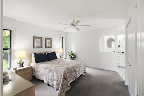 A bedroom with a bed, nightstand, lamp, ceiling fan, and a window.