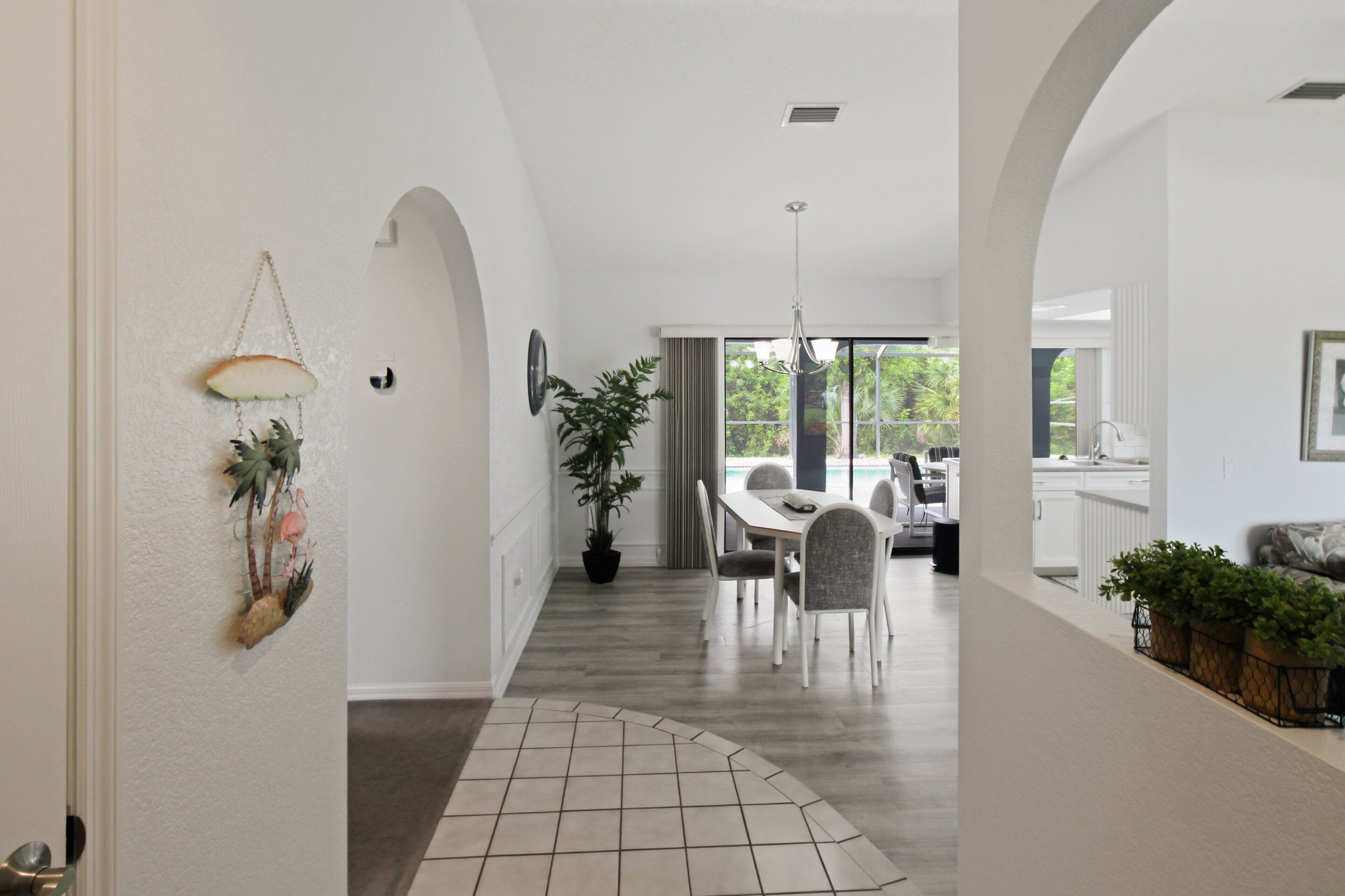 A spacious hallway with a tiled floor, a dining area with a table and chairs, and a view of a pool through large windows.