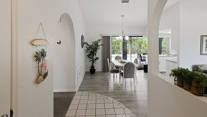 A spacious hallway with a tiled floor, a dining area with a table and chairs, and a view of a pool through large windows. - Relaxing 2BR - Pool home close to attractions - Charlotte's Dream (Port Charlotte)