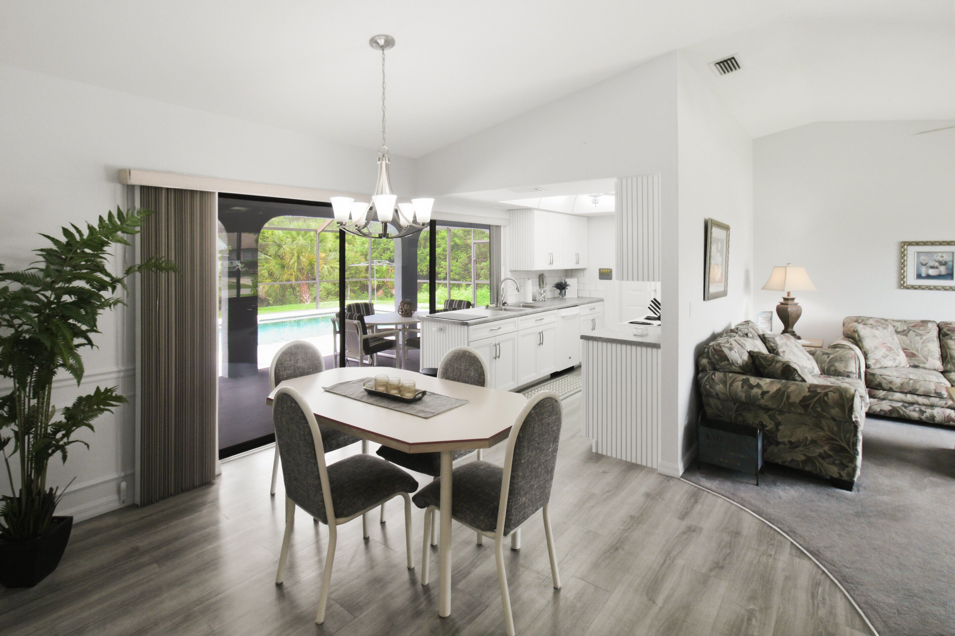 A modern kitchen with white cabinets, a dining area with a table and chairs, and a living room with a couch.