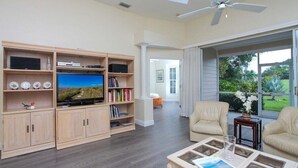 A spacious living room with a large flat-screen TV, wooden cabinets, and a comfortable seating area with two chairs and a coffee table.