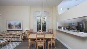 A modern kitchen with a dining area, featuring a chandelier, a sofa, and a painting on the wall.