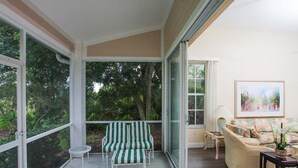 A sunlit room with a sliding glass door leading to a garden, a sofa, and a chair with striped cushions.
