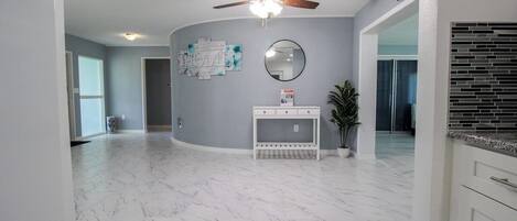 A spacious room with a ceiling fan, a marble floor, a white console table, and a potted plant.