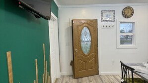 A room with a wooden door, a mounted TV, a clock, and a window with a view. - A  Cozy studio unit in northern Wisconsin (Antigo)