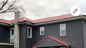 A two-story building with a dark exterior, a red roof, and a central entrance with a wooden door. - A  Cozy studio unit in northern Wisconsin (Antigo)