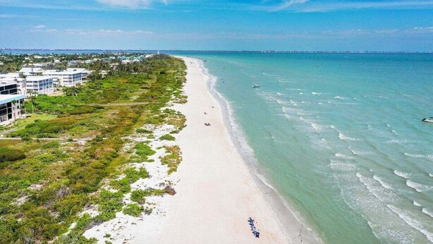 A coastal view with a beach, a white building with multiple floors, and a clear sky. - Spacious 3BR Retreat On Sanibel Island - Steps to the beach - Cyprina Beach #10 (Sanibel)
