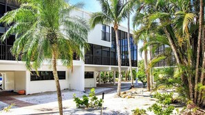 A modern building with a covered outdoor area, palm trees, and a gravel path. - Spacious 3BR Retreat On Sanibel Island - Steps to the beach - Cyprina Beach #10 (Sanibel)