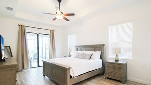 A bedroom with a bed, nightstands, a ceiling fan, and a view through a sliding glass door. - Exquisite waterfront 3BR pool home in Lorraine Lakes - Grand Getaway (Bradenton)