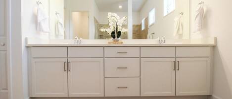 A bathroom with a large mirror, two sinks, and a vanity with drawers.
