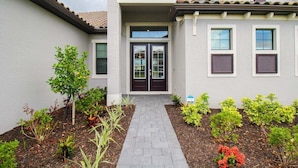 A modern house with a central entrance, a covered porch, and a garden with various plants. - Exquisite waterfront 3BR pool home in Lorraine Lakes - Grand Getaway (Bradenton)