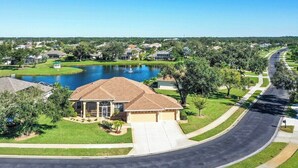 A residential area with a house featuring a large driveway, a pond, and a well-maintained lawn. - Tranquil lakefront pool home in North Port - Rod And Reel (North Port)