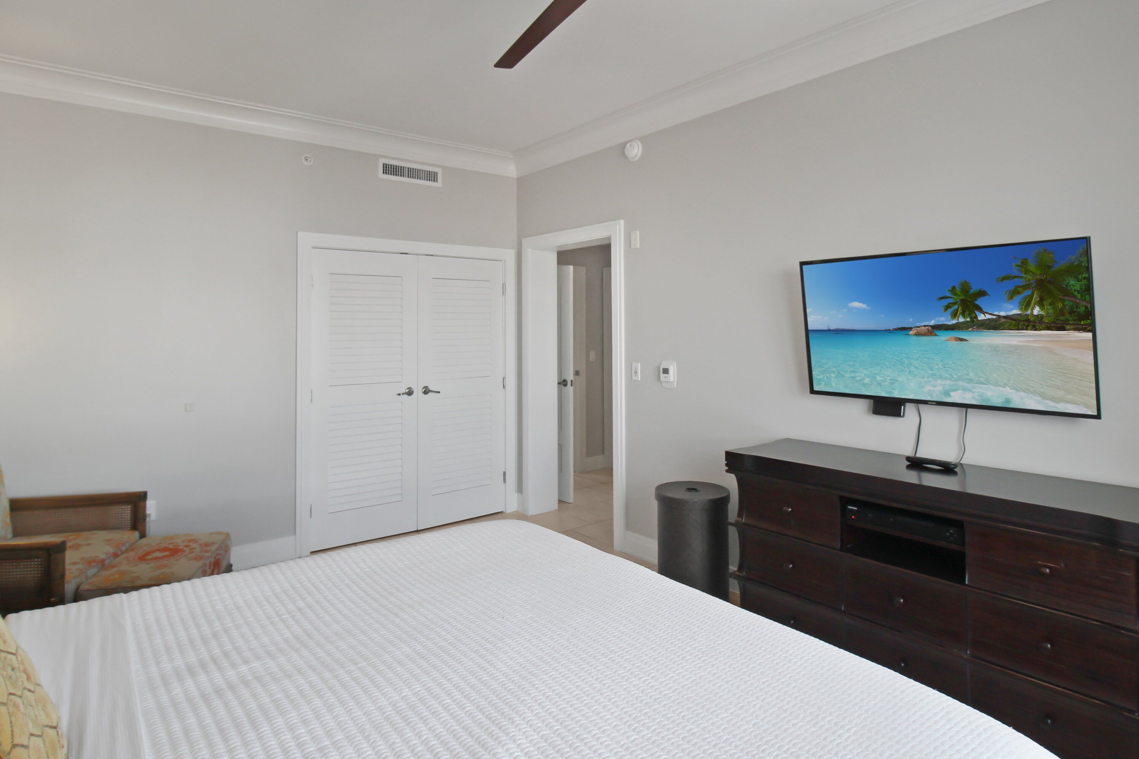 A bedroom with a bed, a television on a dresser, and a door leading to another room.