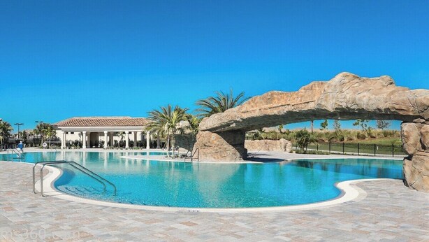 Una piscina con un arco de piedra, palmeras y un edificio al fondo.