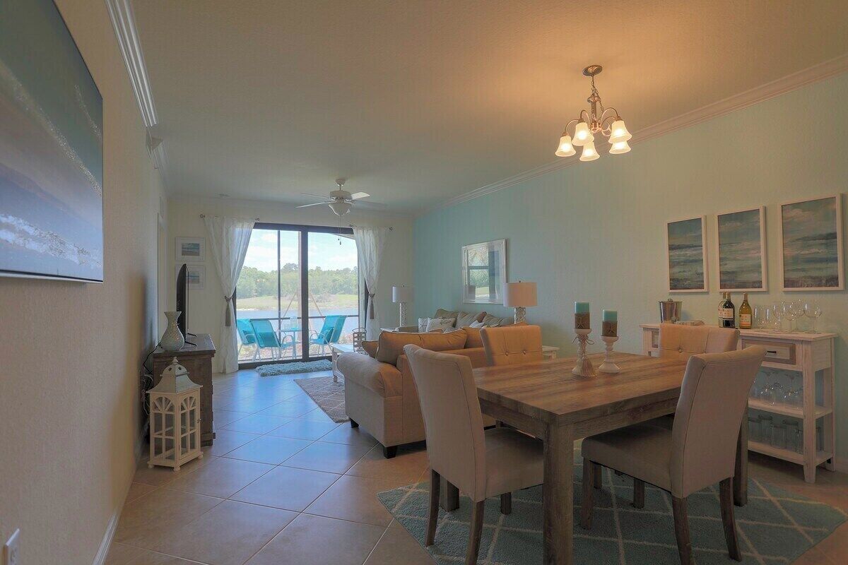A dining area with a wooden table and chairs, a chandelier, and a view of the outdoors.