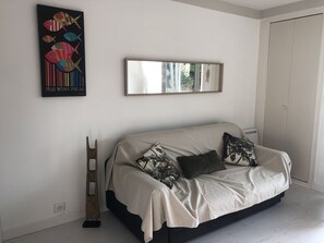 Ein modernes Wohnzimmer mit einer Couch, dekorativen Kissen, einem Wandspiegel und einem farbenfrohen, abstrakten Gemälde.