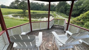 A covered deck with two white Adirondack chairs facing a pond and a grassy field. - Peaceful, spacious 4 bedroom house in the country - Gazebo/Pond
 (Keosauqua)