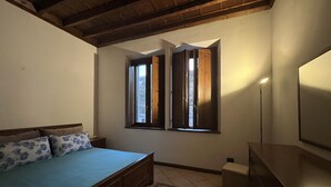 A bedroom with a bed, a nightstand, a dresser, a window with curtains, and a standing lamp.