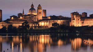 A historic building with a large dome and towers, surrounded by a moat and reflecting in the water.