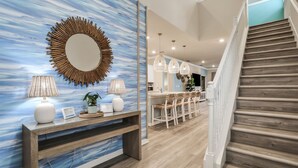 Um interior moderno com escada de madeira, mesa consola com luminárias e parede com espelho circular e um design abstrato azul.