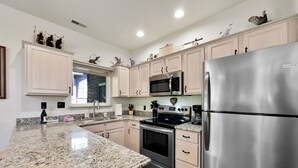 A modern kitchen with granite countertops, stainless steel appliances, and light-colored cabinetry.