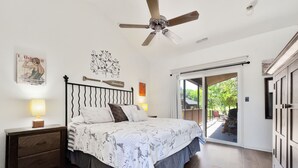 A bedroom with a bed, a ceiling fan, a nightstand, and a view of the outdoors through a sliding glass door.