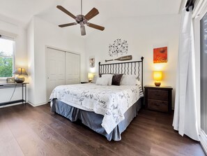 A bedroom with a bed, a ceiling fan, a nightstand with a lamp, a wall clock, and a window with curtains.